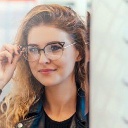 Vrouw past brillen bij de opticien en bekijkt zichzelf in de spiegel terwijl ze een montuur past
